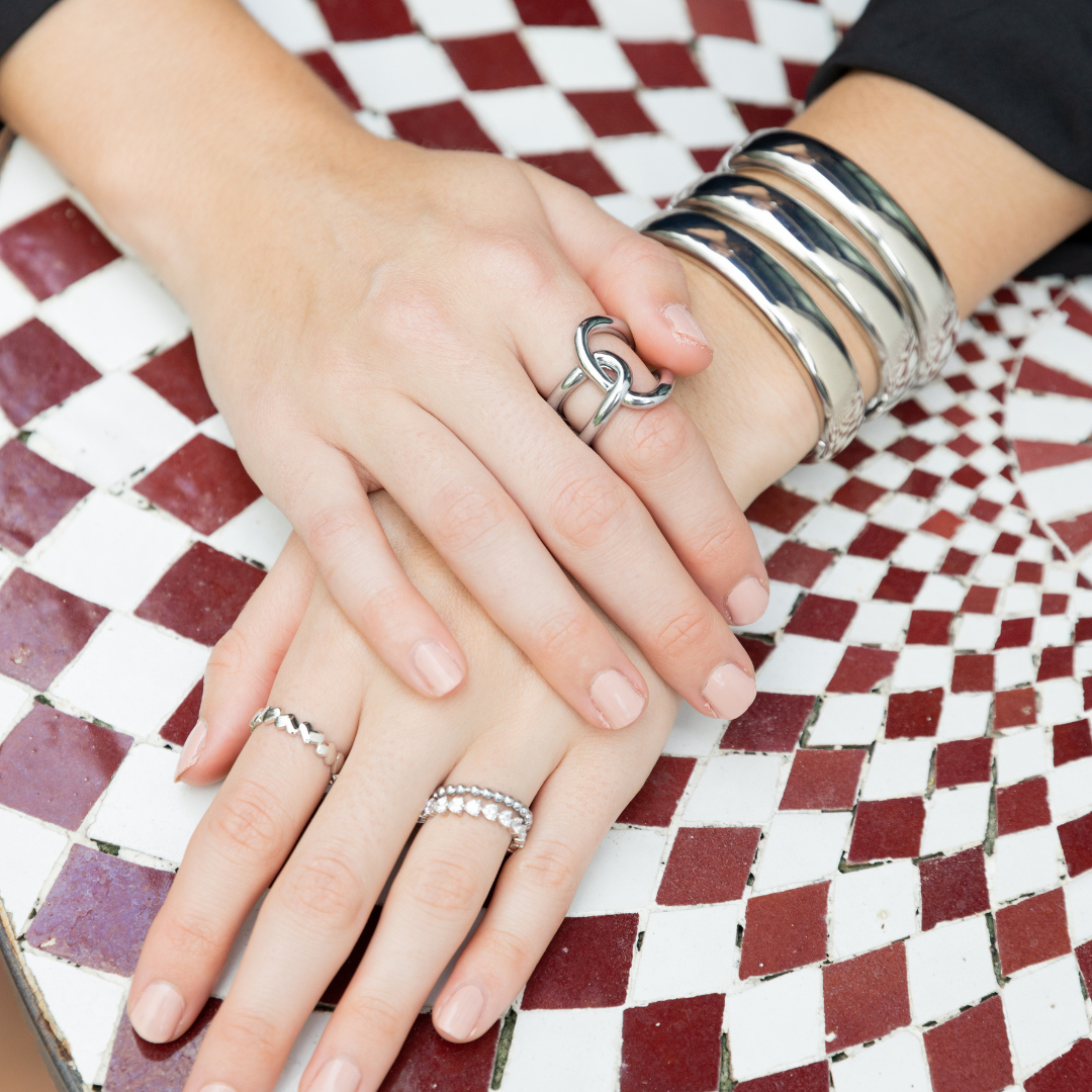 Close-up of hands with silver rings and bracelets on a checkered surface