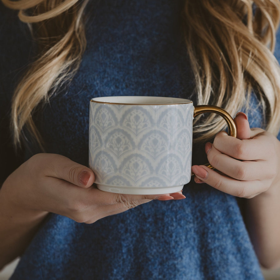 Person holding a patterned ceramic mug with a gold handle