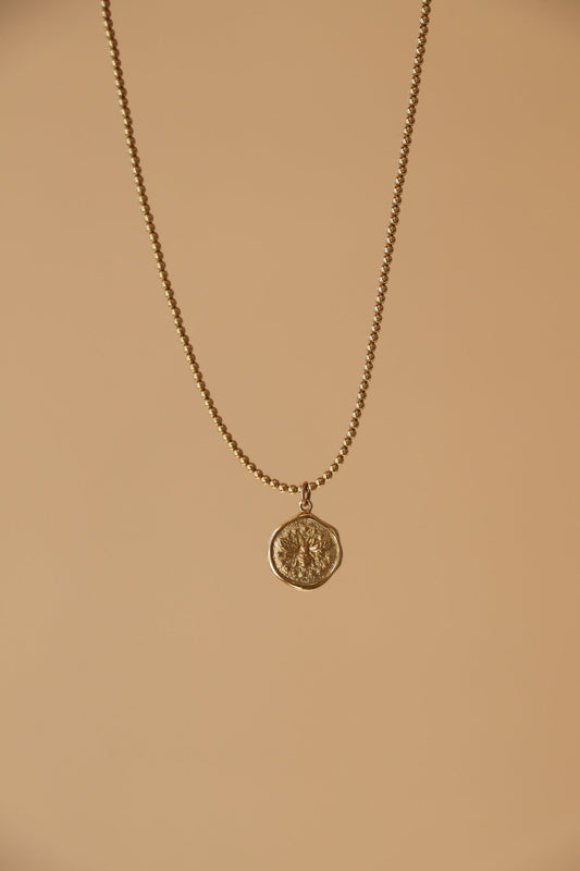 Gold necklace with a wax seal bee charm on a beige background