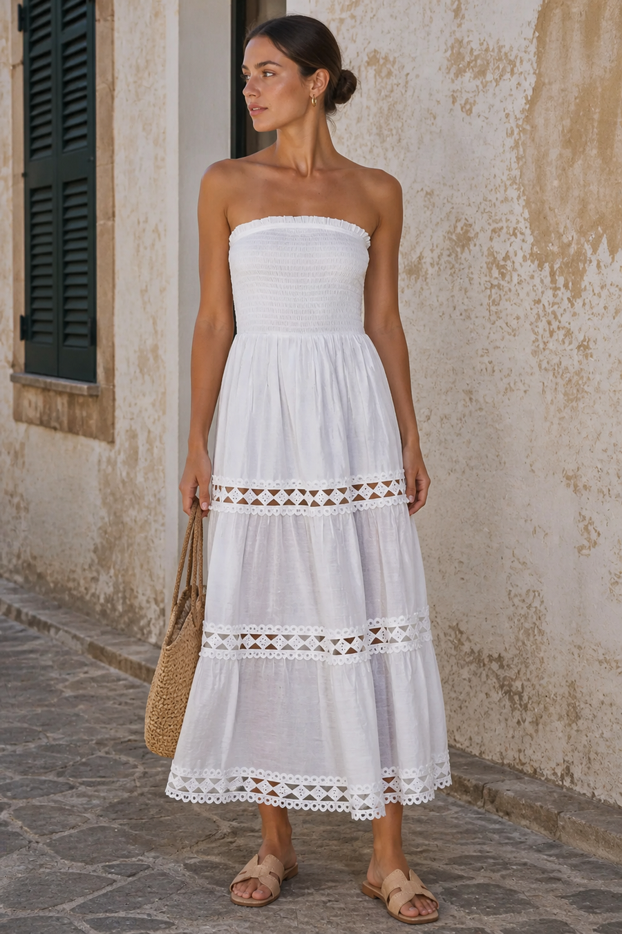A woman wearing a long white strapless maxi dress with a straw bag sold at rosiekarma.com