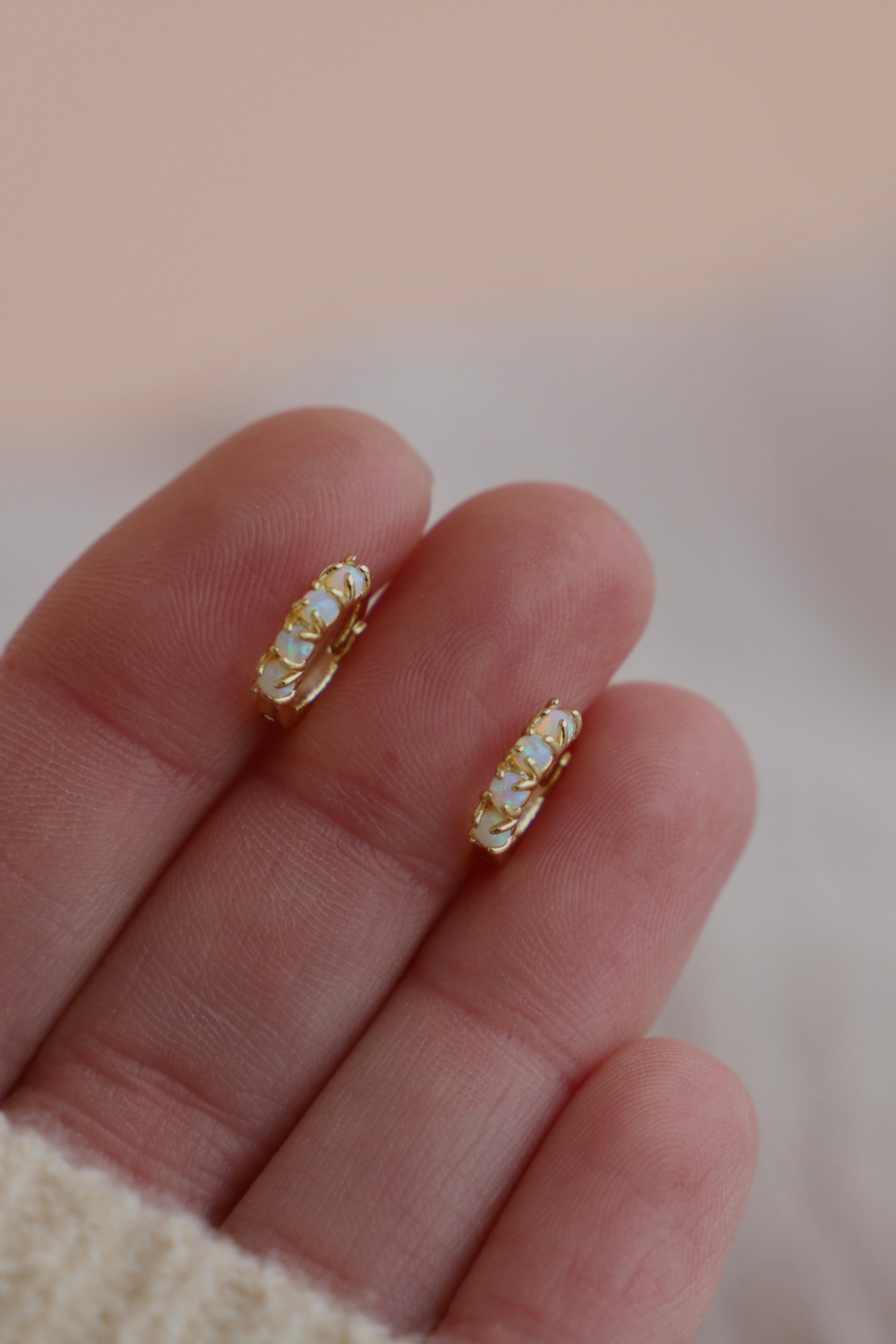 Gold hoop earrings with small stones on a hand against a blurred background