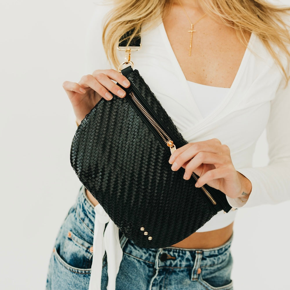Person holding a black woven clutch bag with a white top and blue jeans.