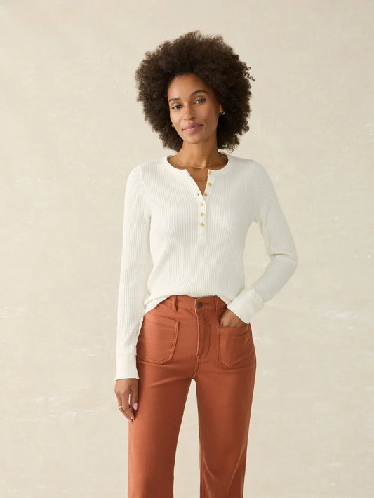 Woman wearing a white ribbed sweater and brown pants against a beige background