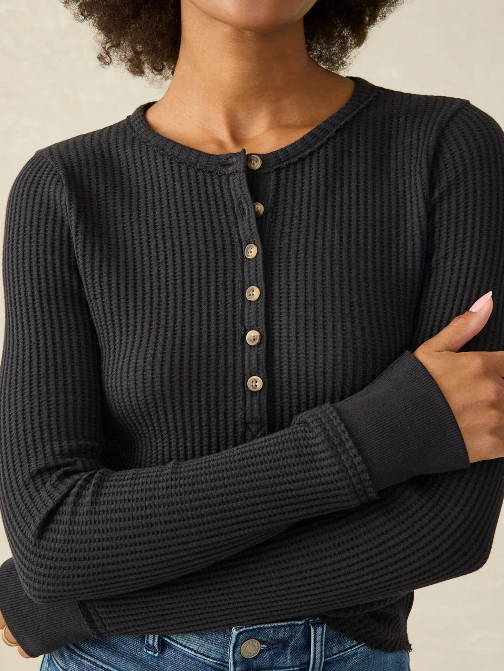Person wearing a black ribbed sweater with button details on a beige background