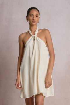 Woman wearing a white halter neck dress against a plain background