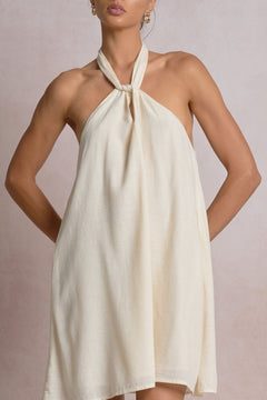 Woman wearing a white halter neck dress against a plain background