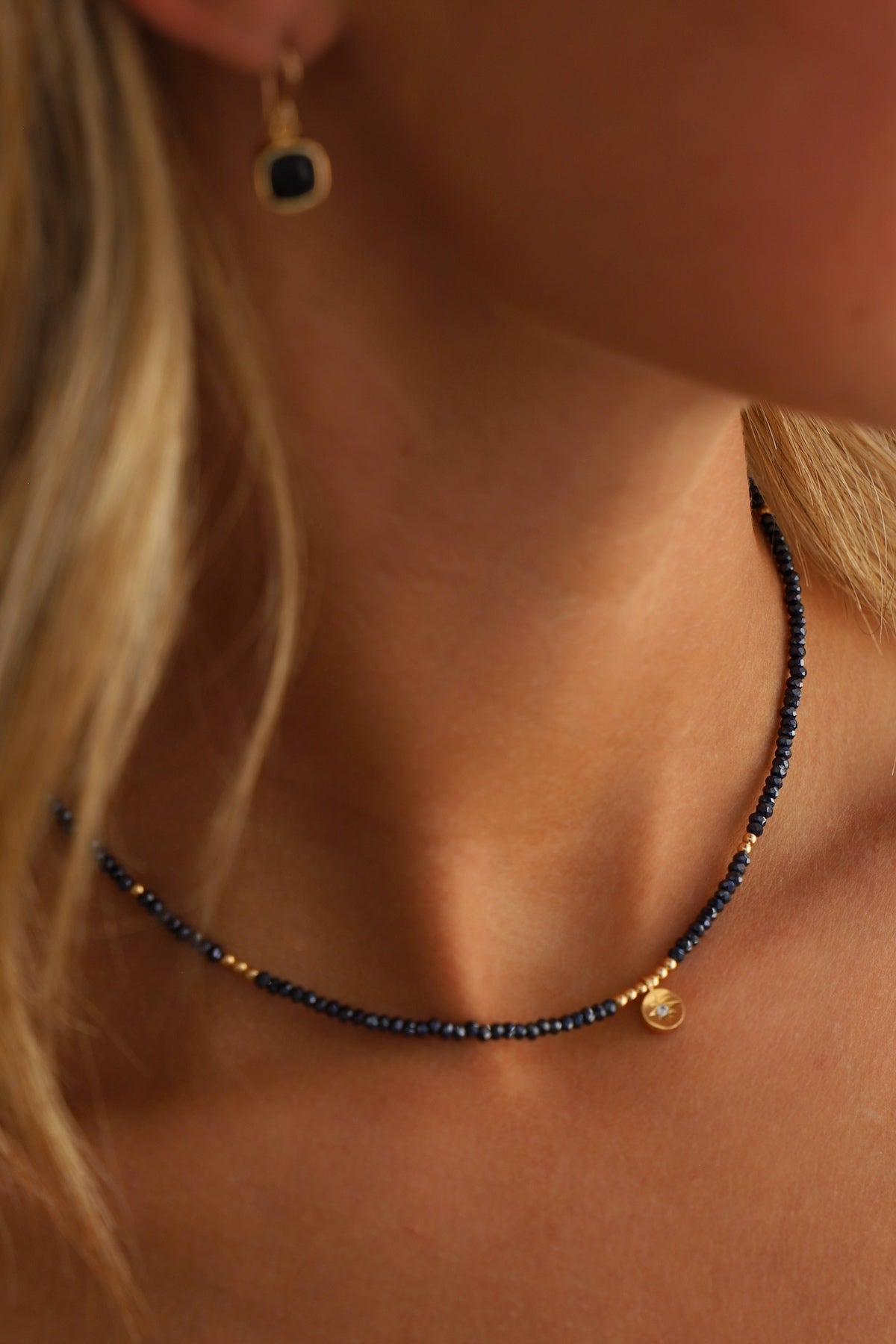Close-up of a necklace with a pendant worn by a person with blonde hair.