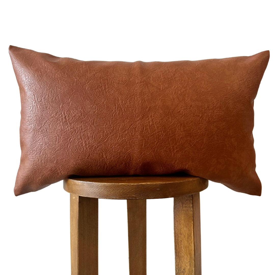 Brown vegan leather pillow on a wooden stool against a white background