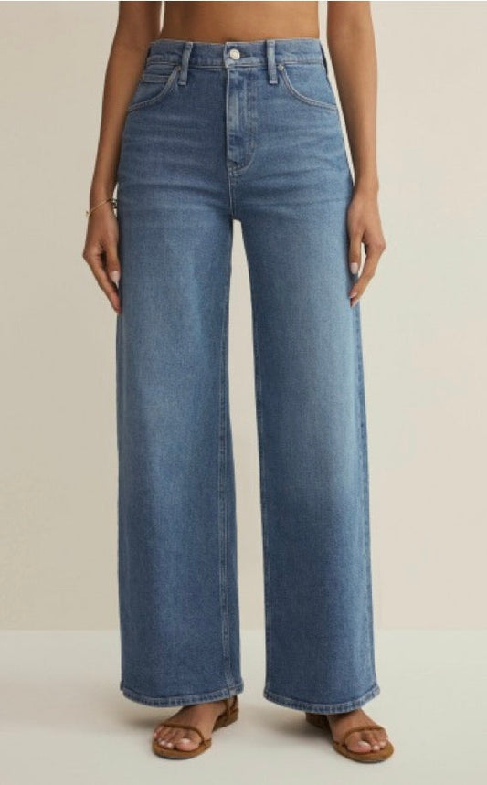 Person wearing blue wide-leg jeans on a beige background