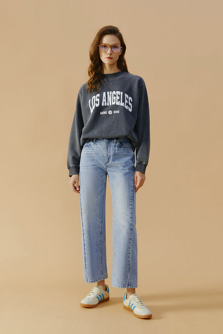 Woman wearing a 'Los Angeles' sweatshirt and jeans on a beige background
