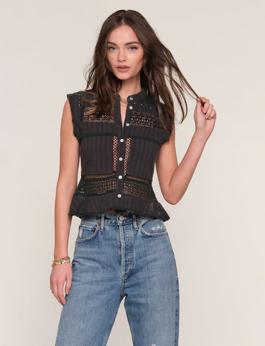 Woman wearing a black sleeveless top with lace details and blue jeans on a beige background