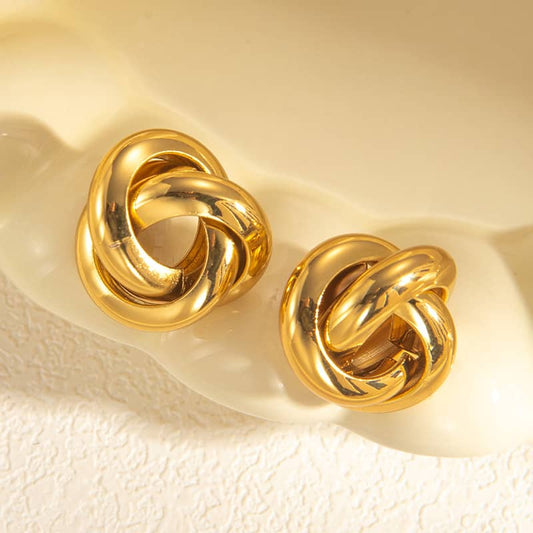 Pair of gold knot earrings on a textured beige surface