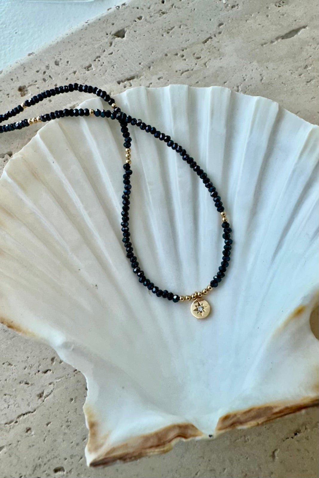 Necklace with black beads and a gold pendant on a white shell