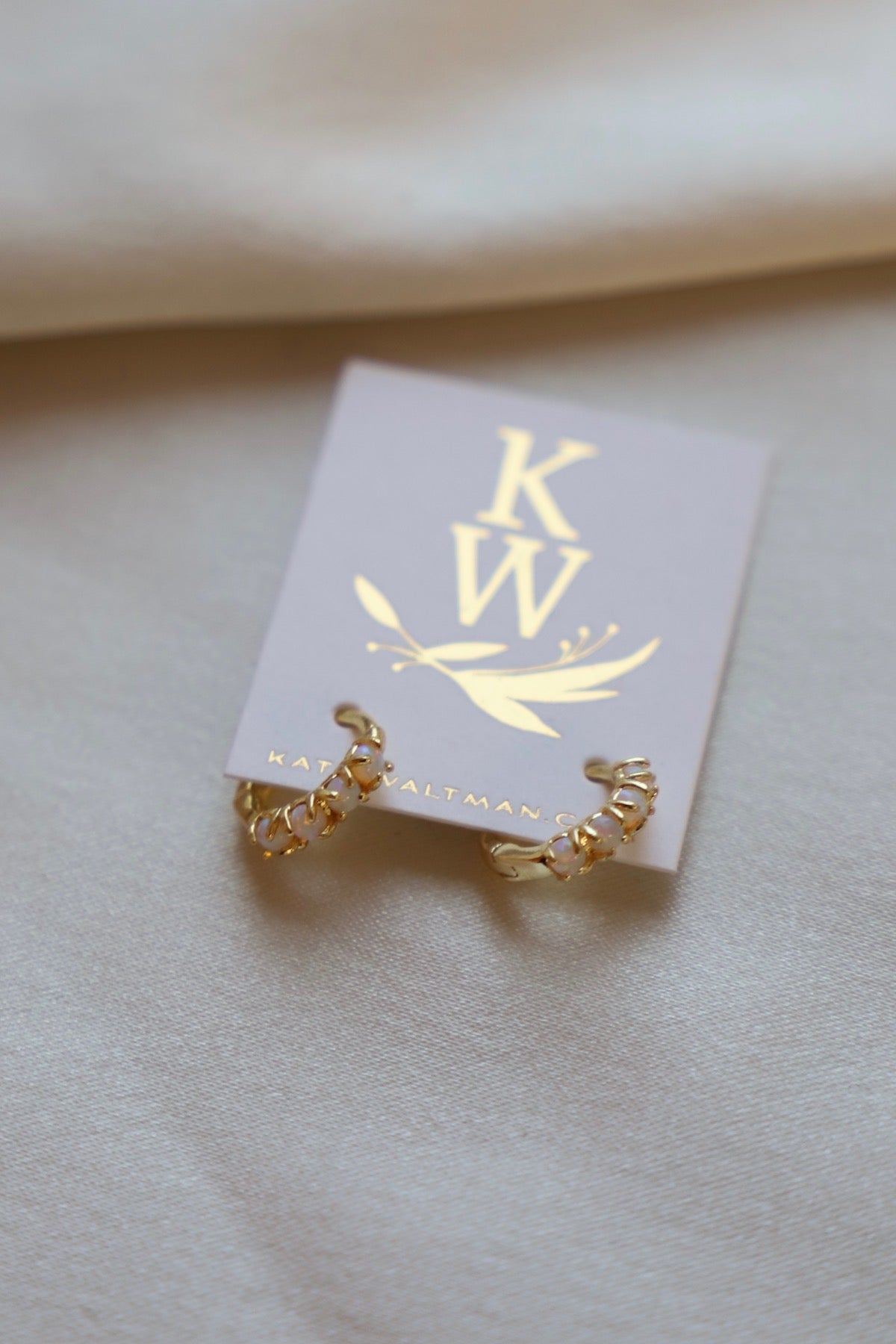 Gold ring on a white card with 'KW' logo on a beige background