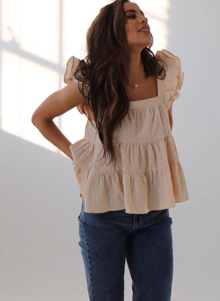 Woman wearing a beige tiered blouse and blue jeans against a white background