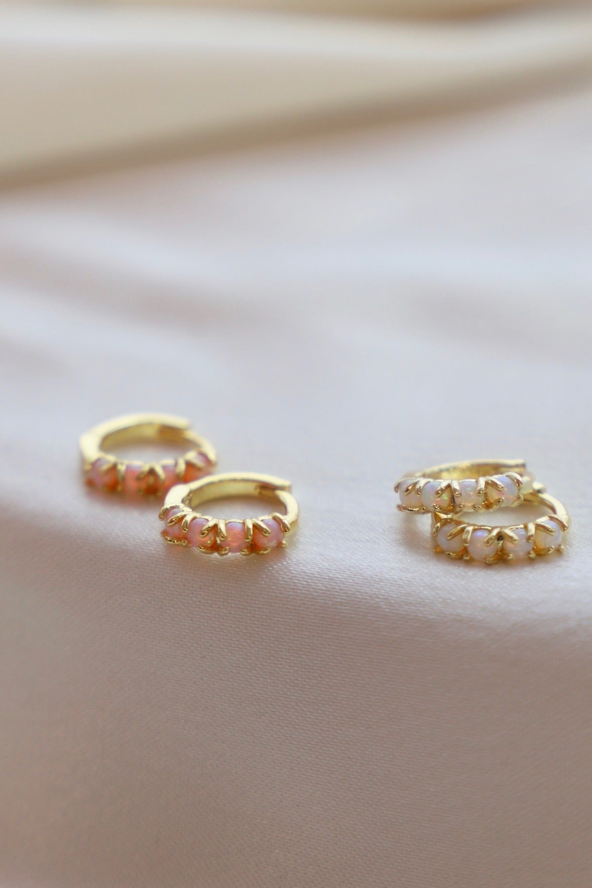 Gold hoop earrings with pink stones on a beige fabric background