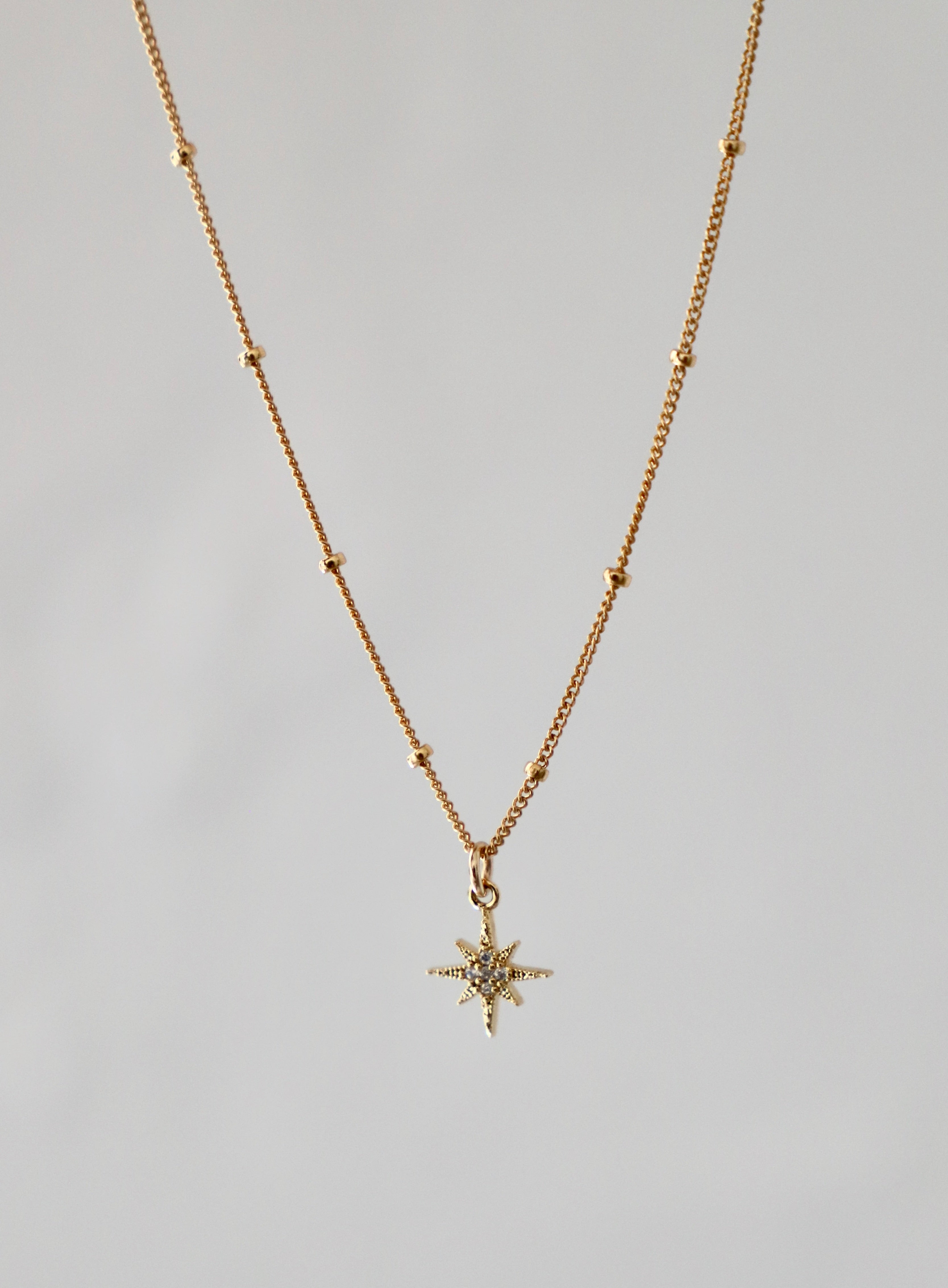 Gold necklace with a star-shaped pendant on a gray background