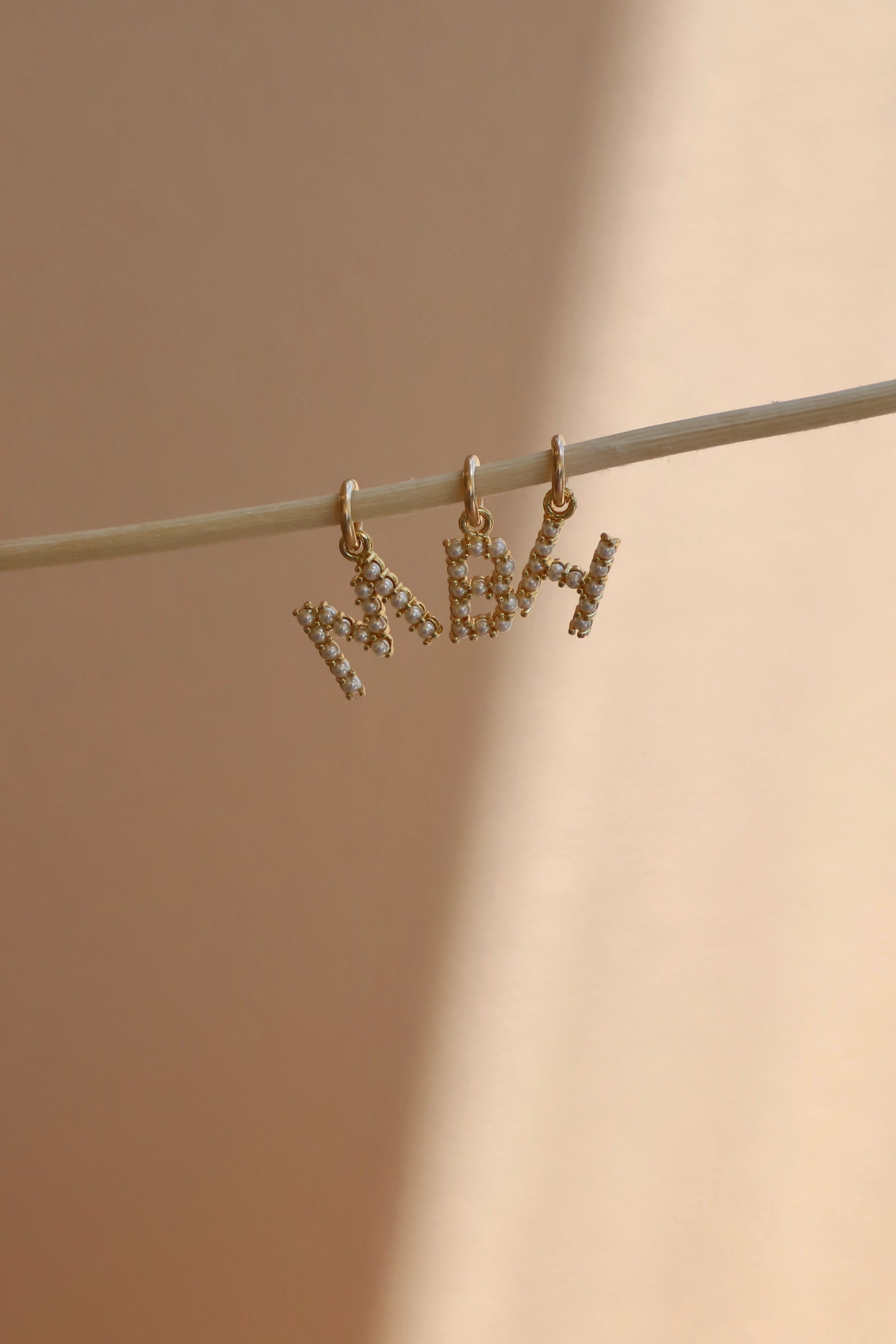 Gold pearl initial earrings with 'MBH' on a beige background