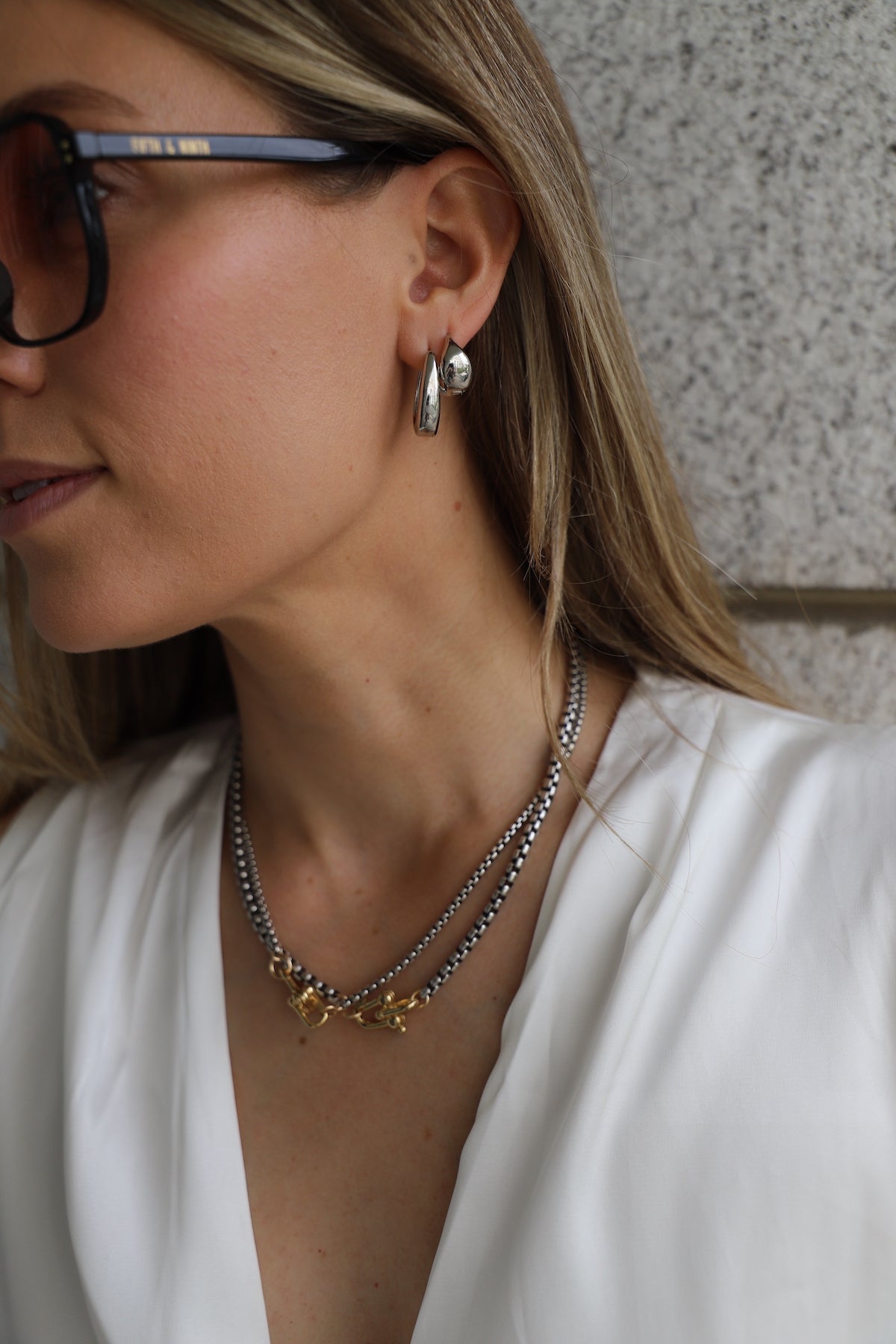 Close-up of a person wearing layered necklaces and earrings with a neutral background