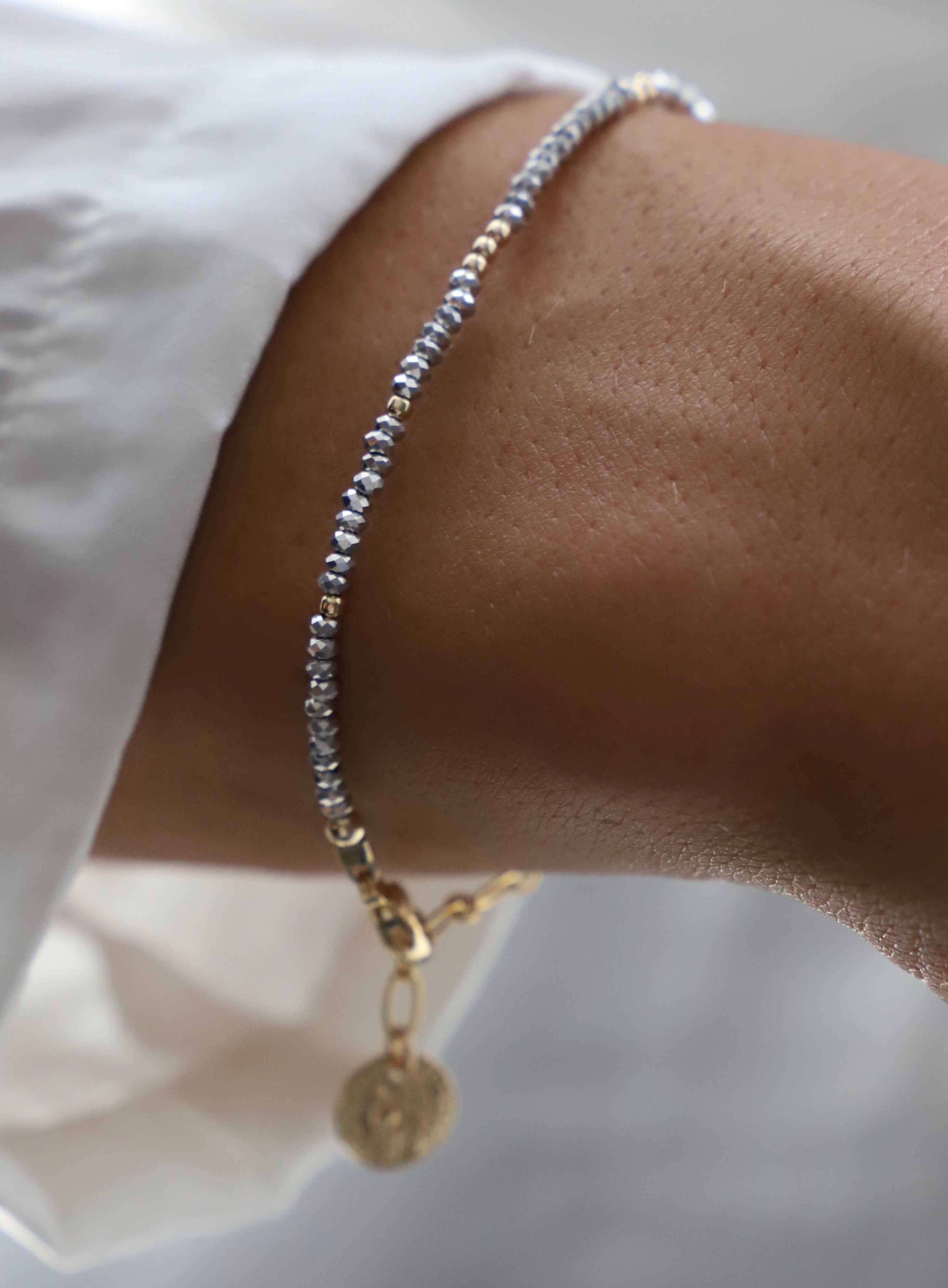 Close-up of a wrist wearing a beaded bracelet with a gold charm on a white background