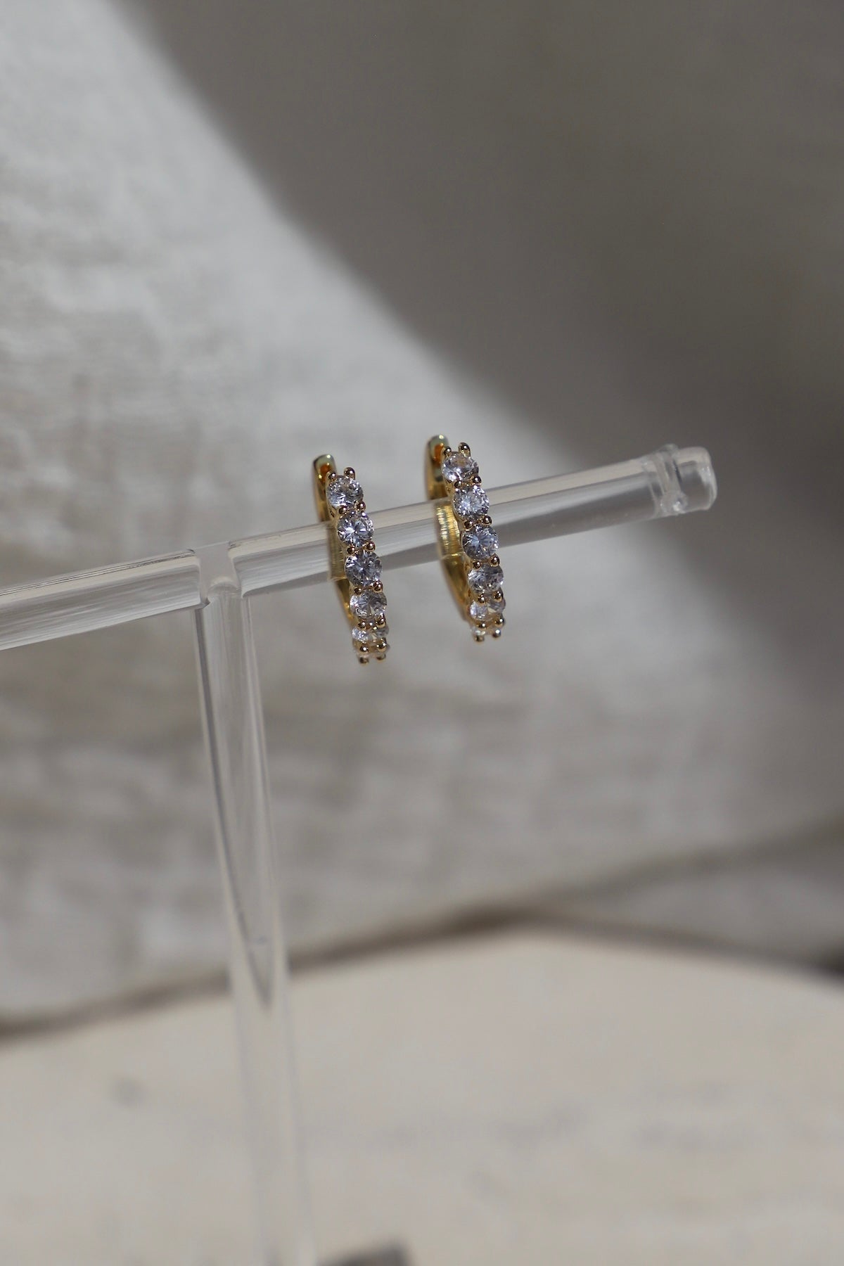 Gold hoop earrings with small diamonds on a clear stand against a neutral background