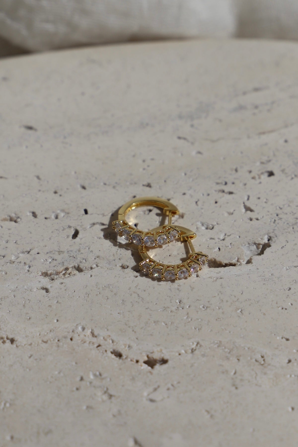 Gold hoop earrings with small diamonds on a textured beige surface