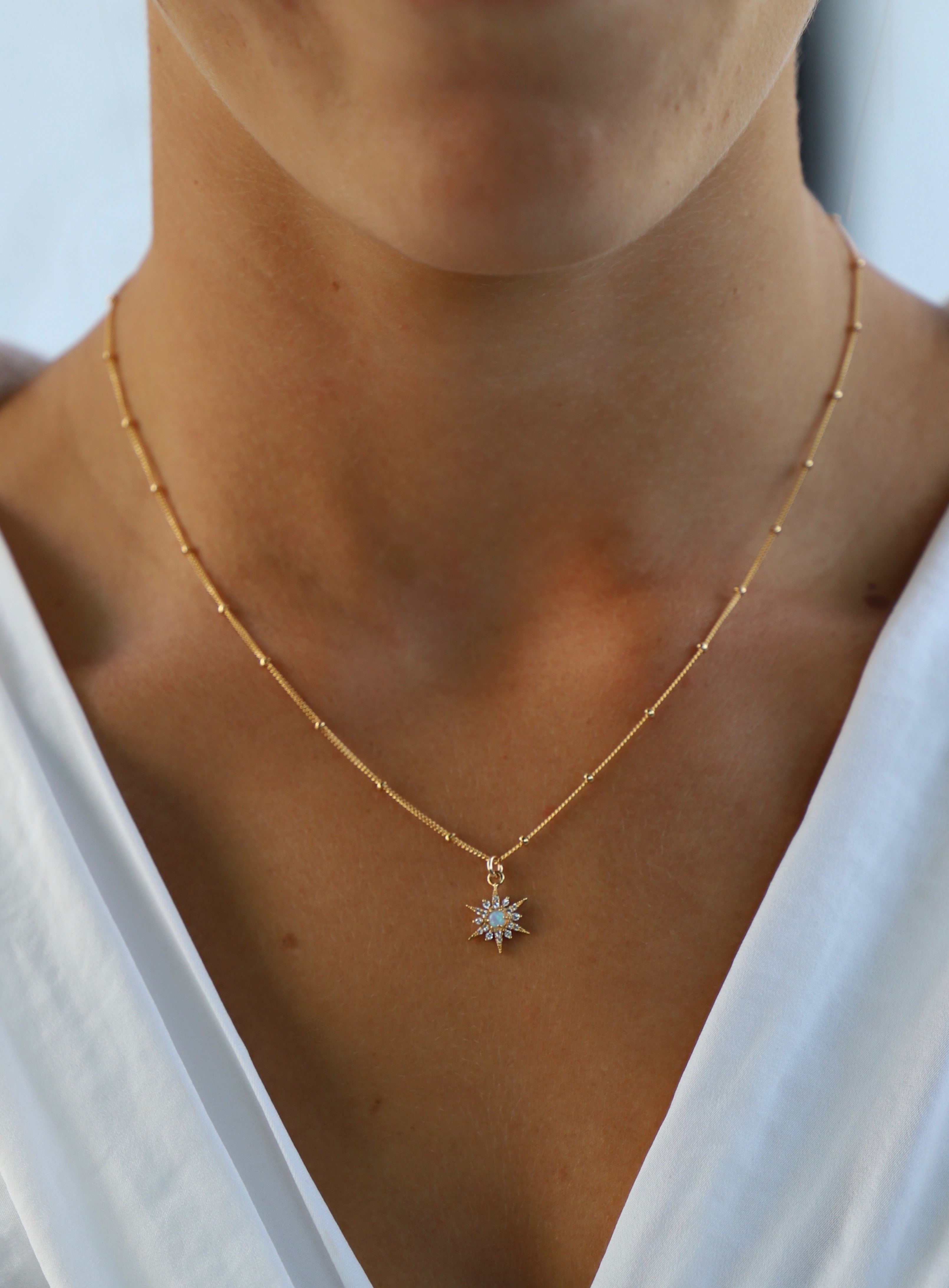 Gold necklace with a star-shaped pendant worn by a person against a white background