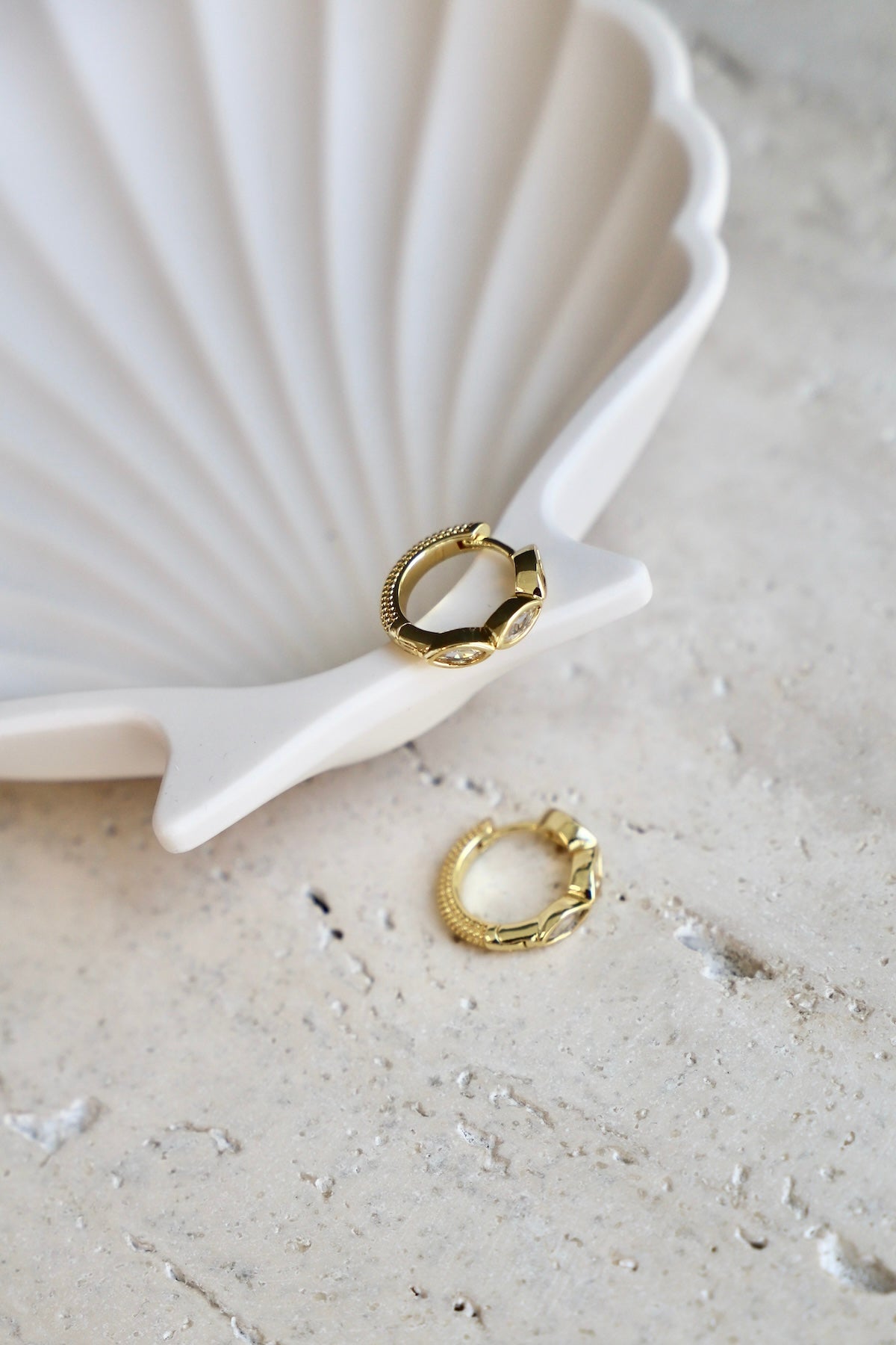 Gold hoop earrings on a textured surface with a shell in the background