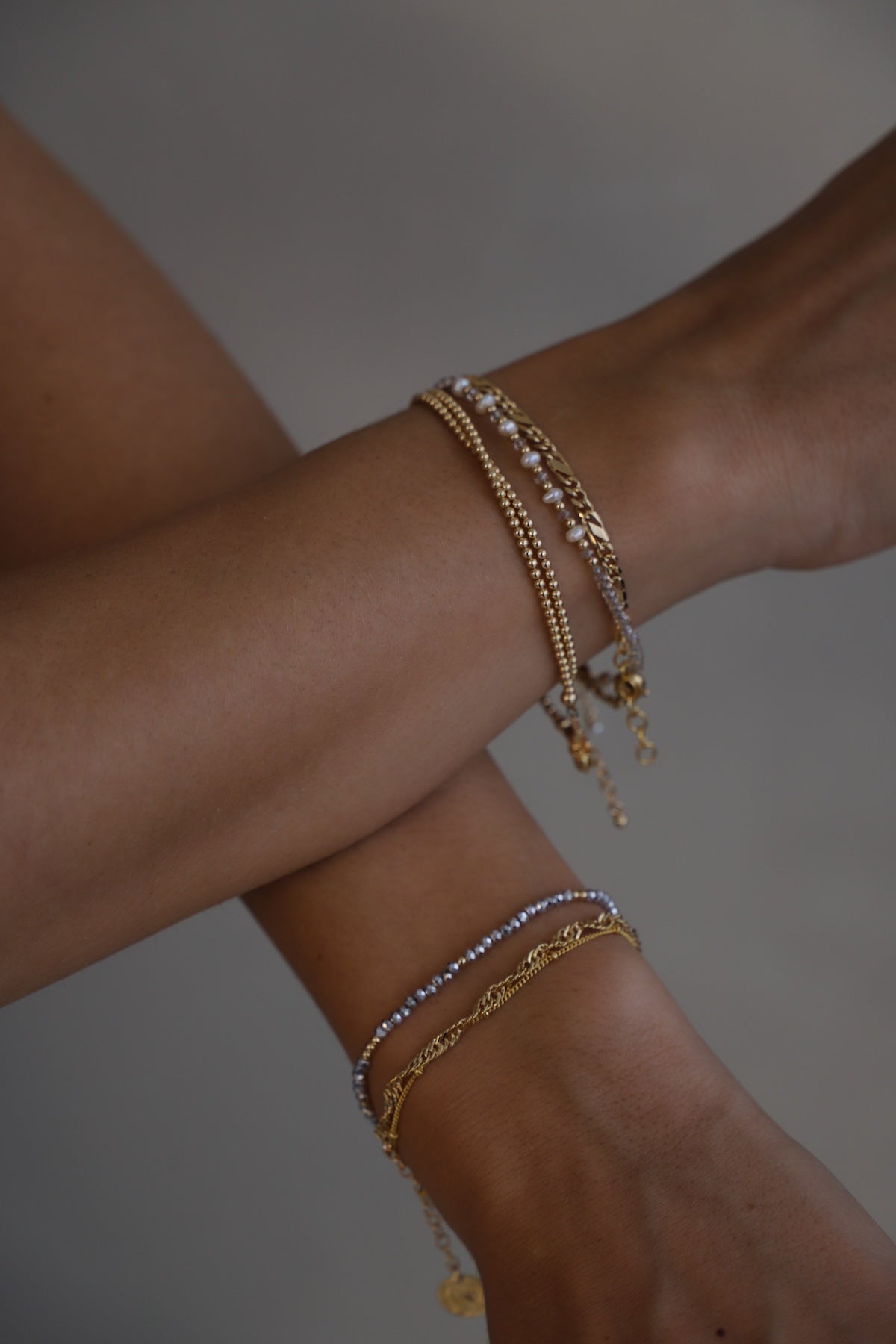 Close-up of a wrist wearing multiple gold and silver bracelets on a neutral background including a Double wrap beaded bracelet in gold filled design – versatile jewelry worn as bracelet or choker necklace, dainty everyday accessory