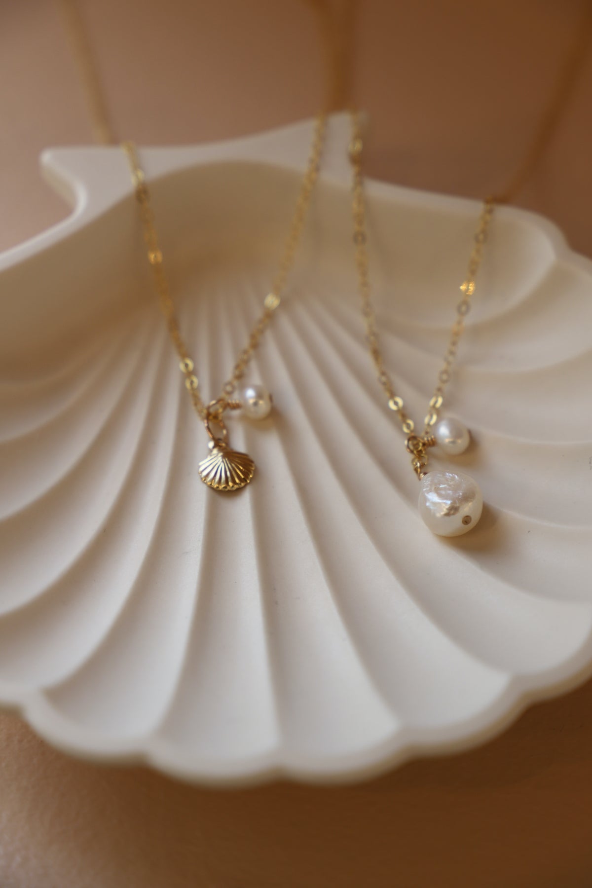 Two gold necklaces with pearls on a white shell