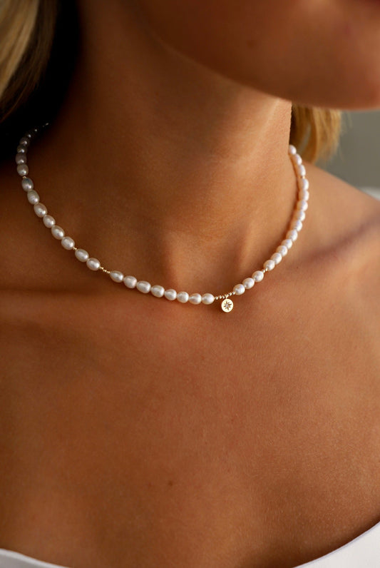 Pearl necklace with a gold charm worn by a person