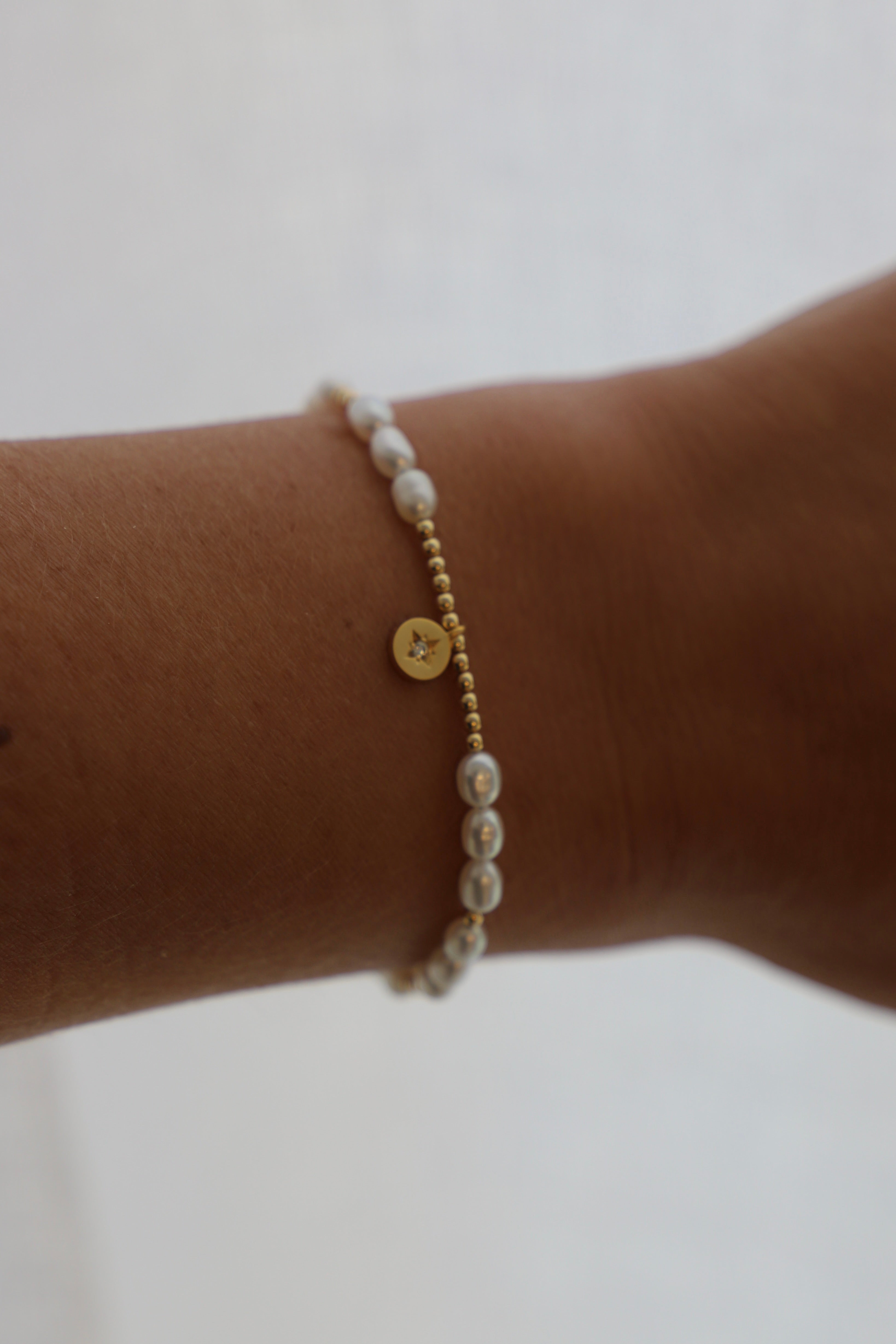 Pearl bracelet with gold accents on a wrist against a light background