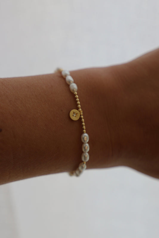 Pearl bracelet with gold accents on a wrist against a light background
