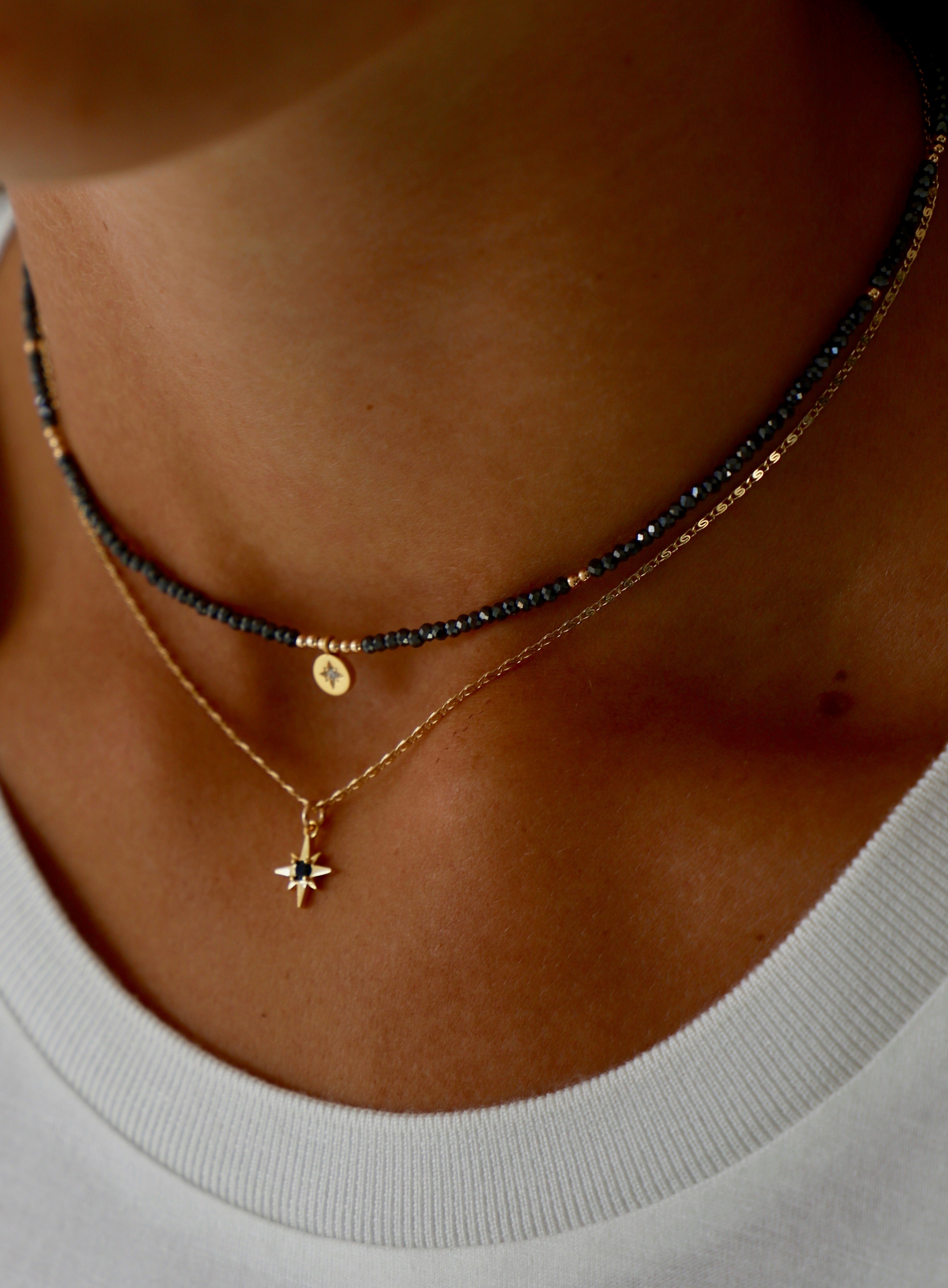 Close-up of a person wearing multiple necklaces with a focus on a gold necklace with a star pendant.