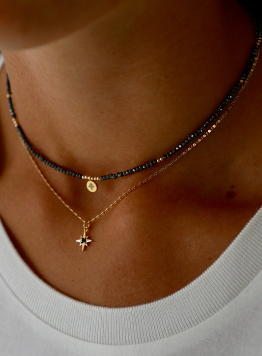Close-up of a person wearing multiple necklaces with a focus on a gold necklace with a star pendant.
