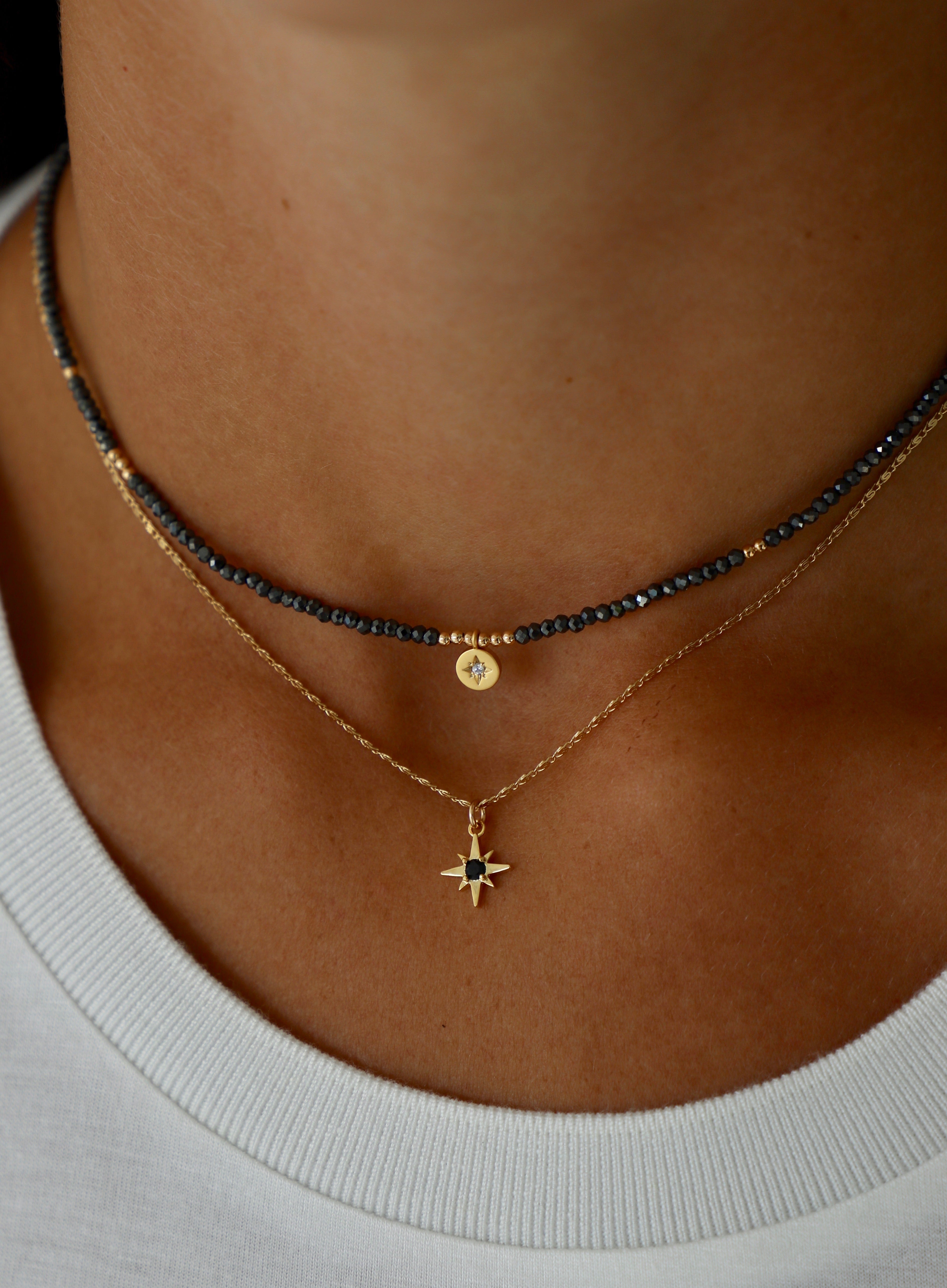 Close-up of a person wearing two necklaces with a star pendant on a neutral background