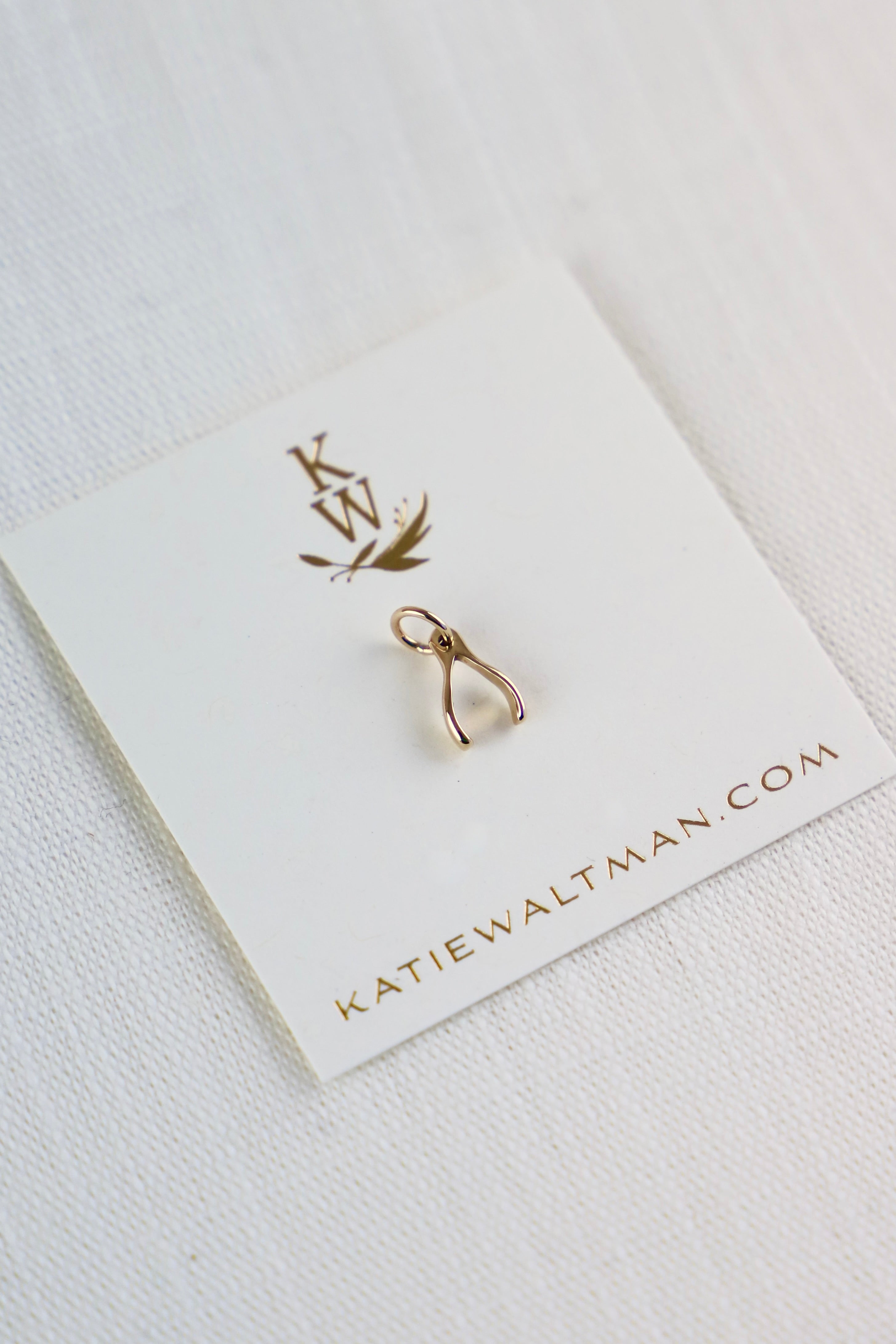 Gold wishbone earring on a branded card with 'katiewaltman.com' on a white background
