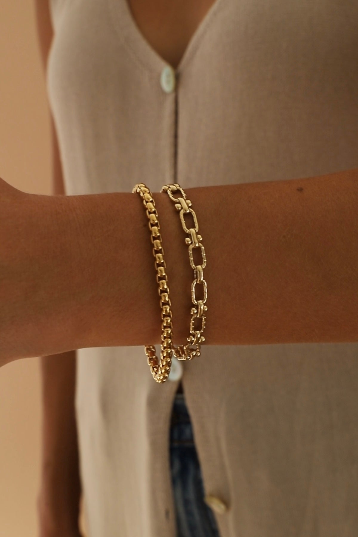 Nova chain bracelet and Gold chain bracelet on a wrist with a neutral background