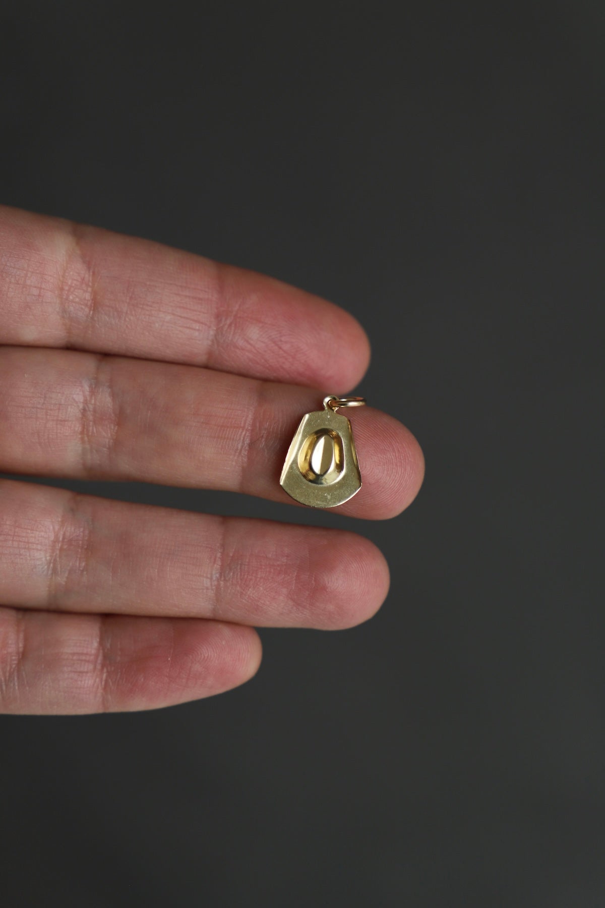 Gold pendant held between thumb and forefinger against a dark background