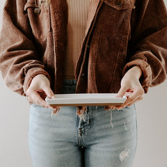 Person wearing a brown corduroy jacket and blue jeans holding a white plate.