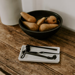 Bowl of pears on a wooden surface with a white container and black tongs.
