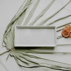 Rectangular white ceramic plate on a light surface with dried orange slices and palm leaves.