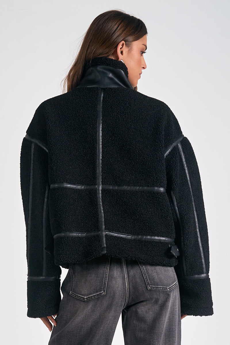 Person wearing a black jacket with leather accents on a white background