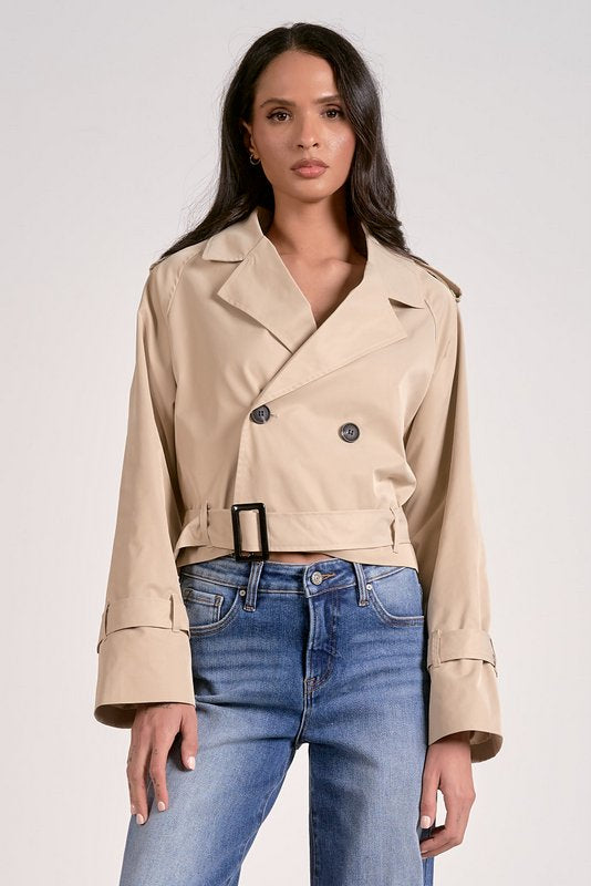 Woman wearing a beige trench coat and blue jeans on a white background