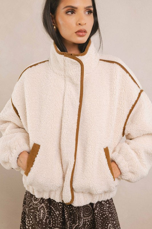 Woman wearing a cream-colored fleece jacket with brown accents on a plain background