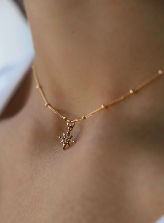 Gold necklace with a star-shaped pendant on a person's neck