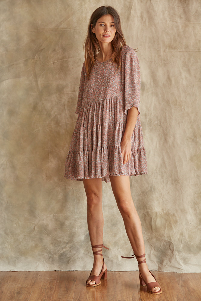 A woman wearing a short sleeve, knee-length brown chiffon dress with a round neckline and ruffle detailing.