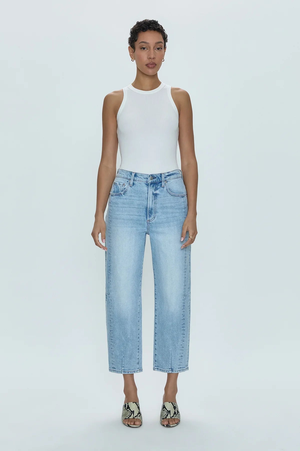 Woman wearing a white tank top and light blue jeans on a plain background