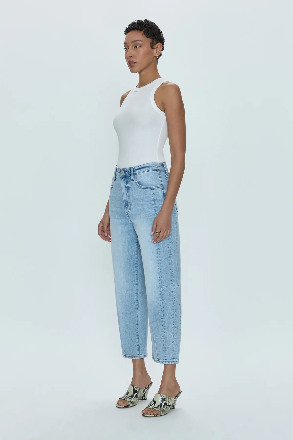 Woman wearing a white sleeveless top and light blue jeans on a white background
