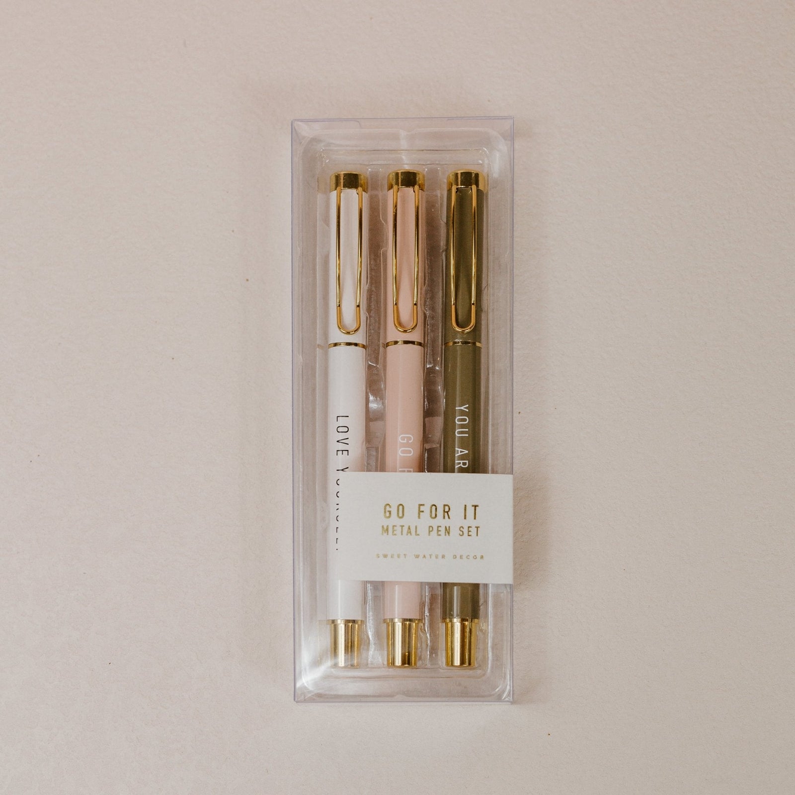 Set of three pens in clear packaging with gold accents on a beige background